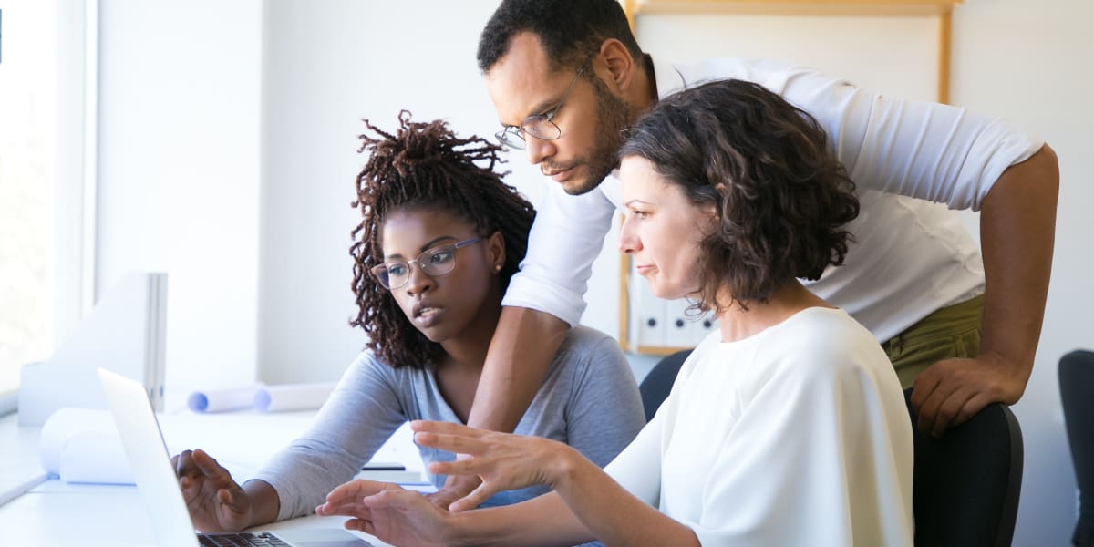 Bootcamps with the Best Mentorship and Support A UX design mentor sitting at a desk, talking to two mentees about their work