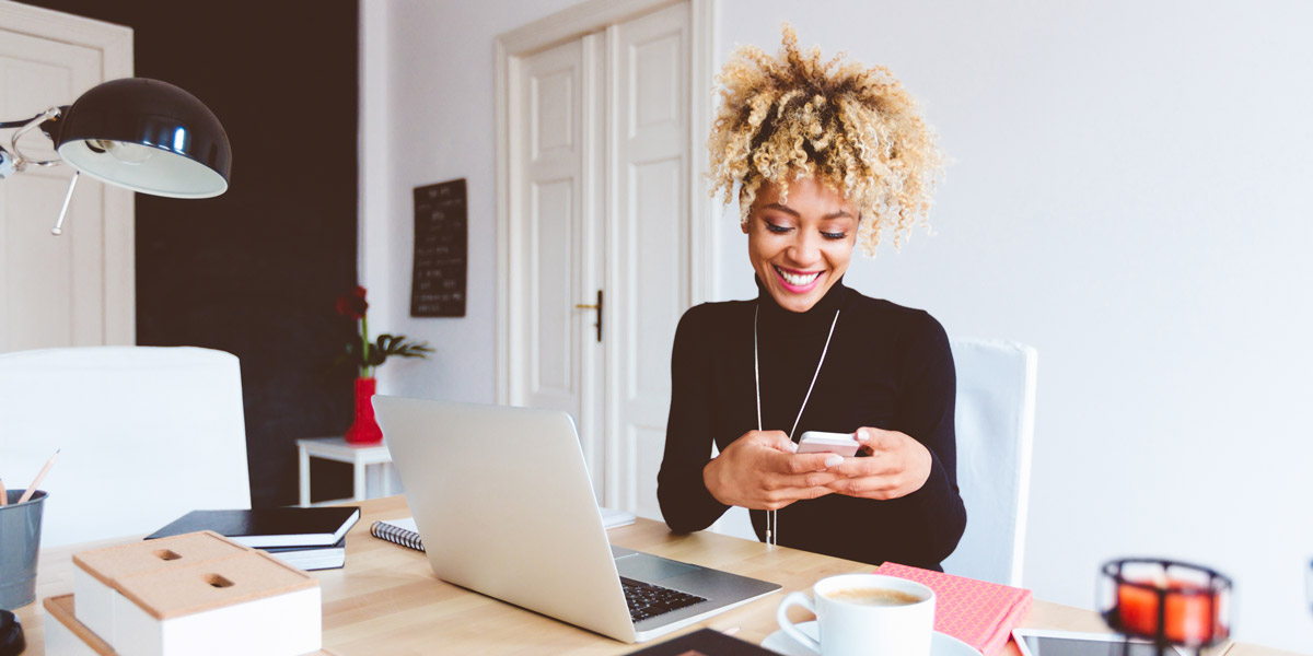 How to Get Started in UX Design An aspiring UX designer sitting at a desk with a laptop and cup of coffee, working on her phone