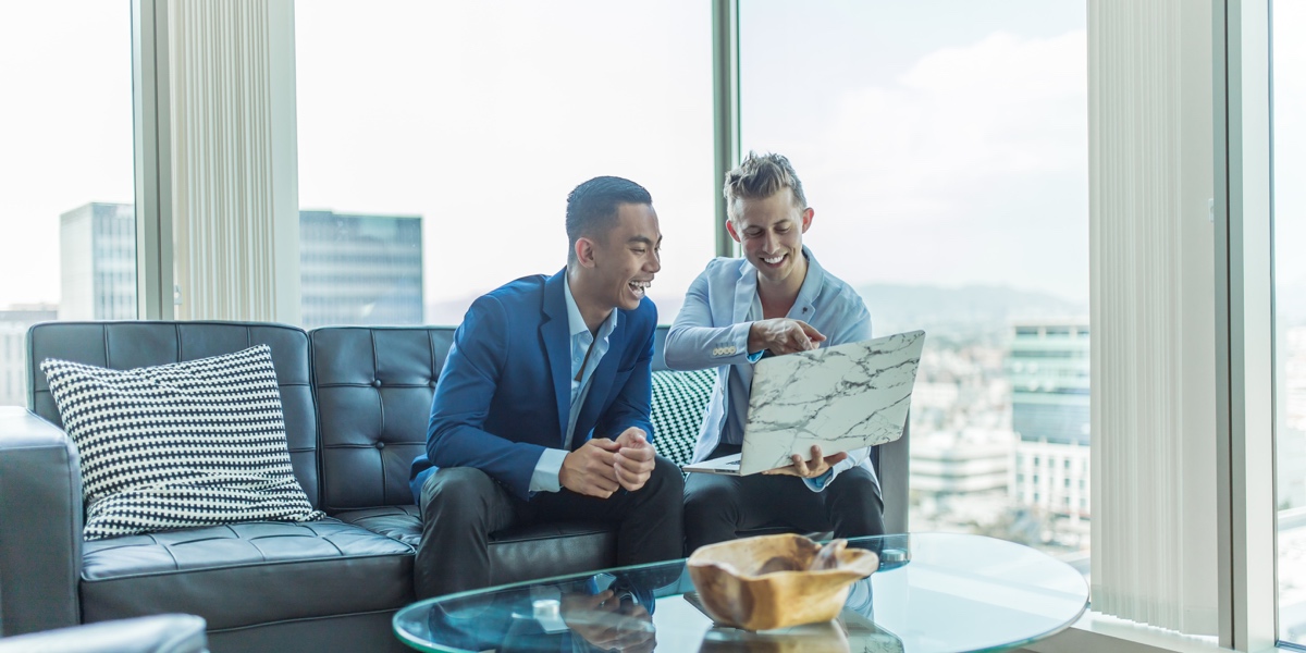 Two UX researchers sitting on a couch near a large window, looking at data on a laptop