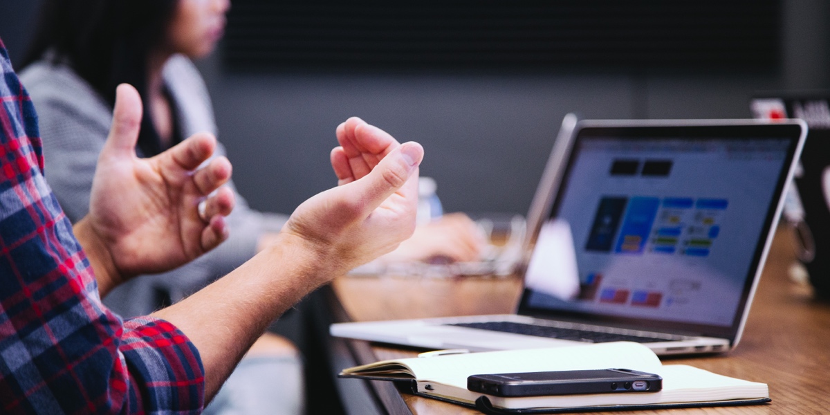 Close up of a UX researcher's hands. They are working at a laptop with a phone and open notebook nearby