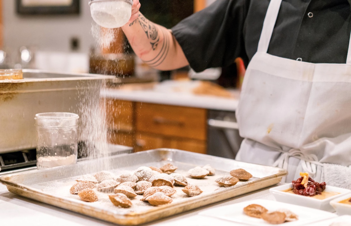 Baker sifting powder over creations on a tray