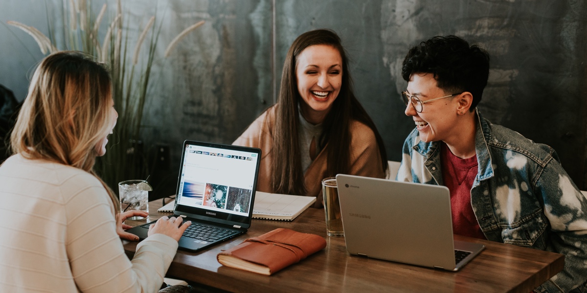 The Power of Storytelling in UX Three people gathered at a cafe table with laptops, laughing and talking