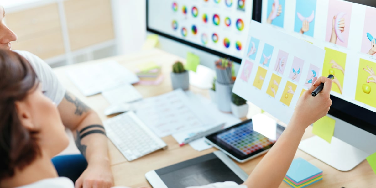 Two UI designers sitting at a desk, looking at graphics on a computer screen