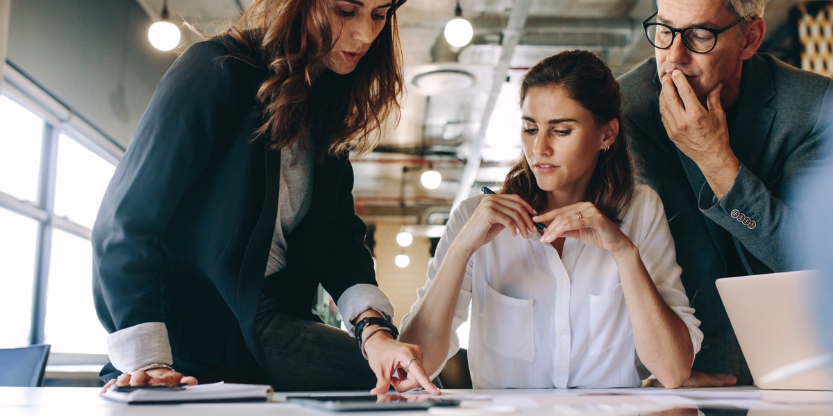 Three UX designers gathers at a desk looking at their UX strategy