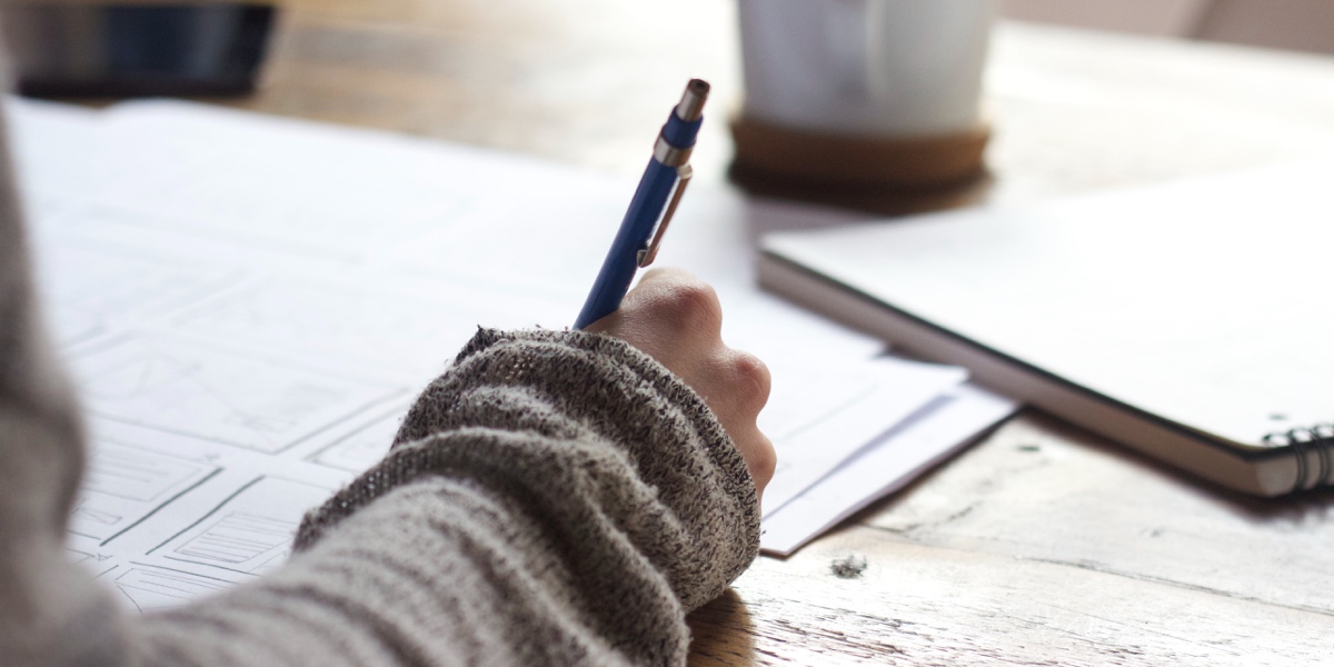 Resources to Learn UX Writing Close-up of a writer's hand, holding a pen and scribbling notes