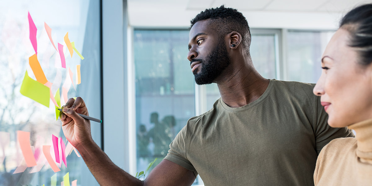 Two designers working at a glass wall covered in sticky notes