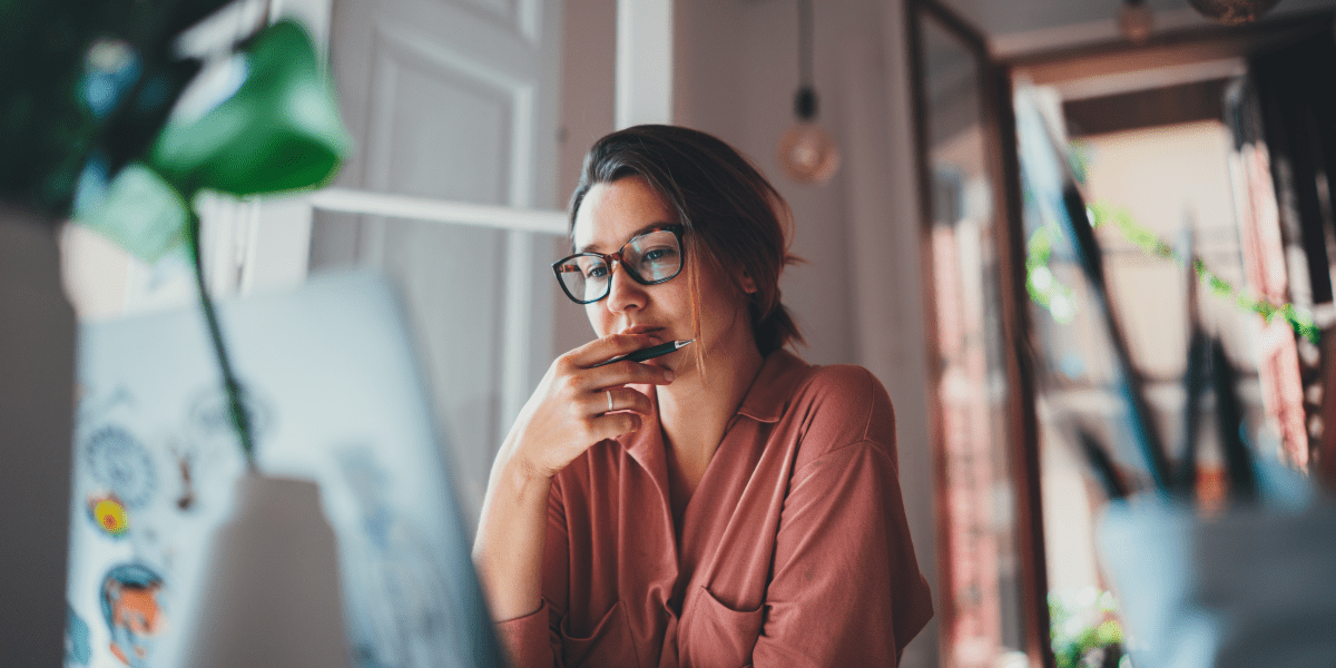 Female web developer sitting in her office office working at her computer with a book open next to her.