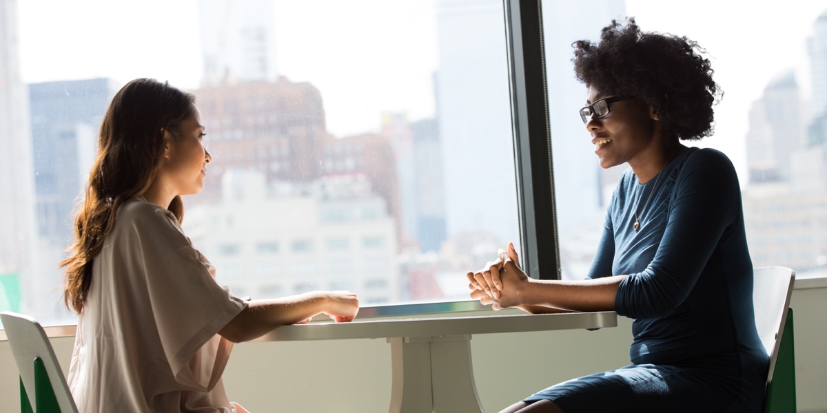 Two women sitting at a table near a large window, in conversation